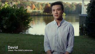 Young man named David, identified as a client of The Child’s Advocate, sits outdoors near a lake with trees in the background, speaking to the camera.
